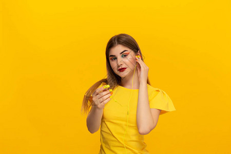 身穿黄色T恤的快乐年轻模特用站在黄色背景上的有线耳机听图片
