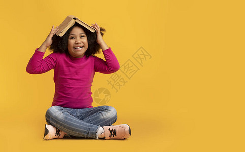 有张头坐在黄色背景的公开书籍的玩耍非洲女孩的肖图片