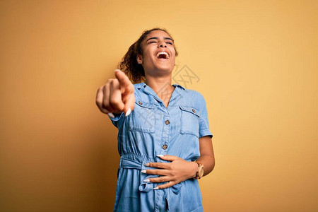 年轻漂亮的非洲裔美国女孩穿着牛仔裙站在黄色背景上嘲笑你图片