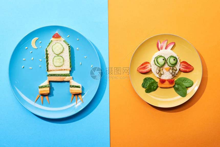 蓝色和橙色背景的儿童早餐用食物制成的带有花哨的脸和火箭的盘图片