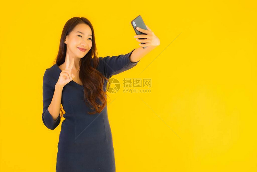 拥有智能手机或手机黄色孤立背景的漂亮年轻女图片