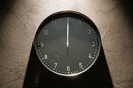 中心的黑色简单模拟时钟特写显示午夜挂在深棕色的墙上图片