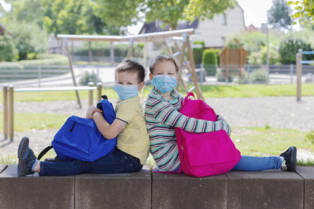 带着一套装的弟或女孩和男孩坐在外边学校操场上图片