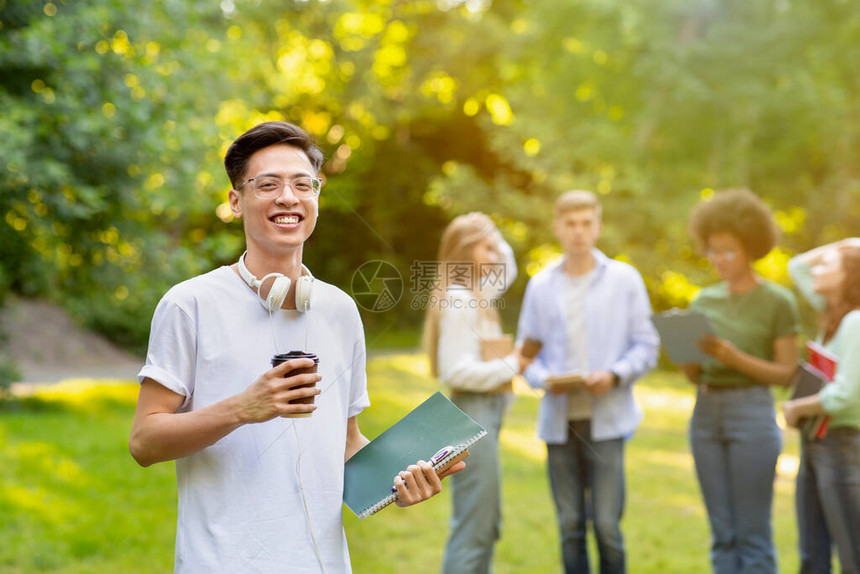 微笑的亚洲男学生拿着外送咖啡在户外摆姿势图片