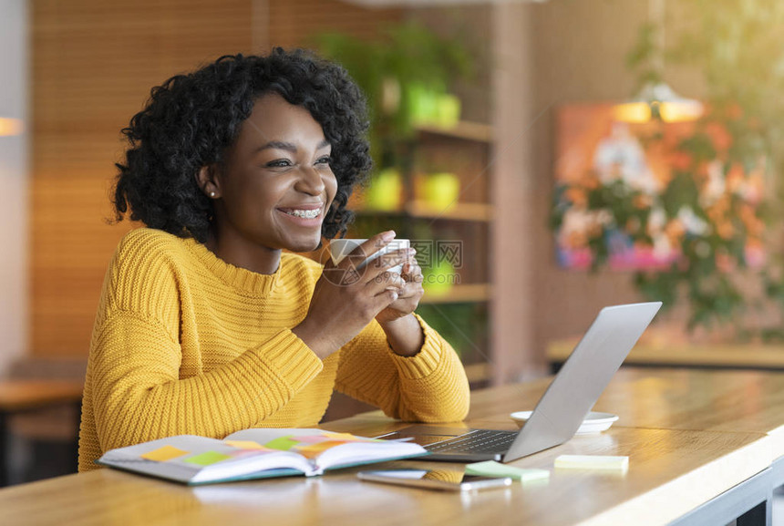 兴奋的非洲女孩喝茶使用笔记本电脑记笔寻找新工作机会咖啡馆内部图片