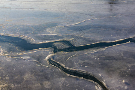 温暖早春河海的薄冰被裂缝覆盖着阳背景图片