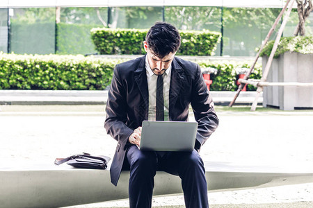 穿着黑色优雅西装的英俊商人坐着用笔记本电脑工作图片