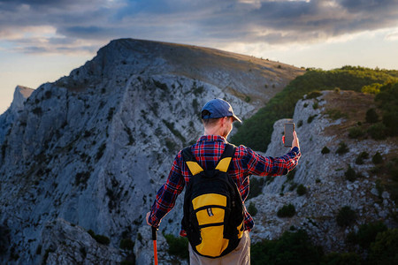 强壮的男子徒步旅行者在山峰用智能手机拍照奇妙的黎明活动的概念和移动图片