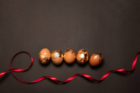 深色背景中金棕色鸡蛋和红色丝带的最小组成图片
