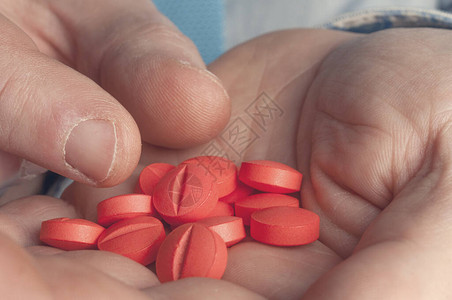 医生的手拿药丸用满红色药丸的图片