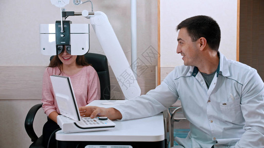 眼科治疗年轻微笑的女人用验光设备检查她的视力坐在附近图片