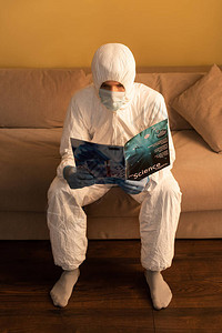 穿着哈兹马特西装和医疗面具阅读科学杂志的男子图片