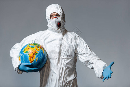 身穿哈兹马特西装和医疗面具的男子持有着地球图片