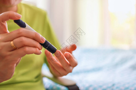 早上用手指上的柳叶刀在卧室里用血糖仪检查血糖水平的人手的特写用作医学糖尿病血糖保背景图片