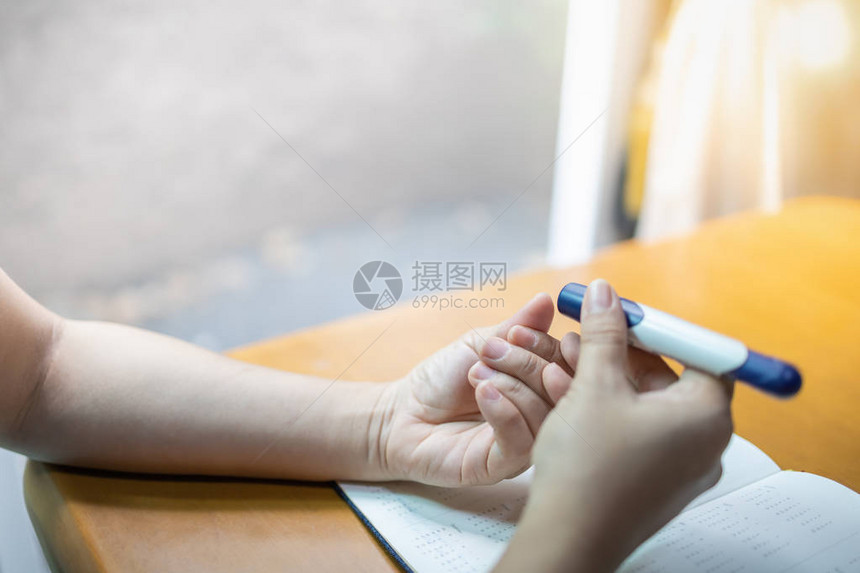 用手指上的柳叶刀用血糖仪检查血糖水平的女人手的特写图片