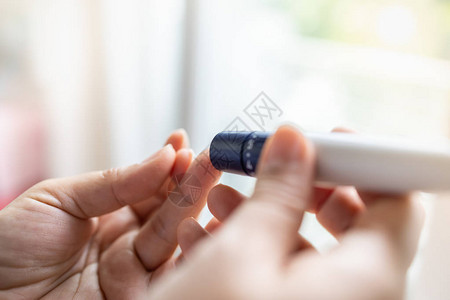 用手指上的柳叶刀在早上用血糖仪检查血糖水平的女人手的特写用作医学糖尿病血糖保背景图片