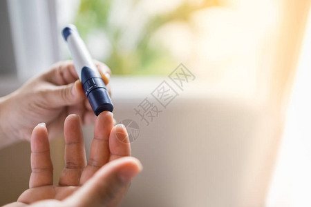 用手指上的柳叶刀在早上用血糖仪检查血糖水平的女人手的特写用作医学糖尿病血糖保背景图片