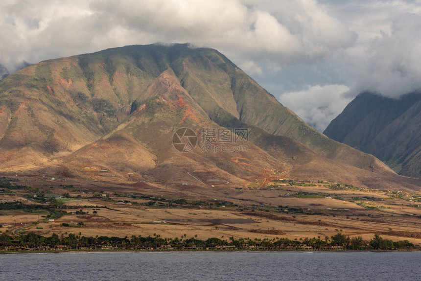 浓云下的绿褐色山峰哈雷阿卡拉火山范围的一部分前面靠近海滩和灰色海洋的棕色图片