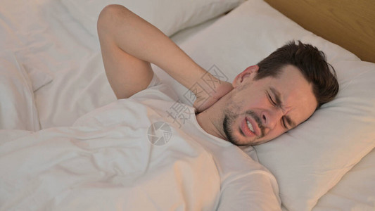 疲倦的年轻人在床上颈部疼痛图片