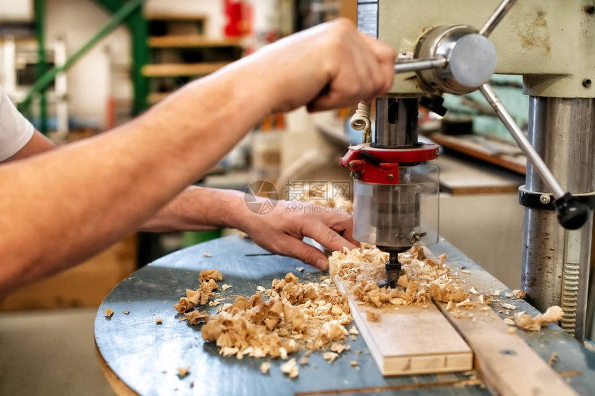 木工或木匠使用垂直钻头在木工车间用木屑在木块上钻孔图片
