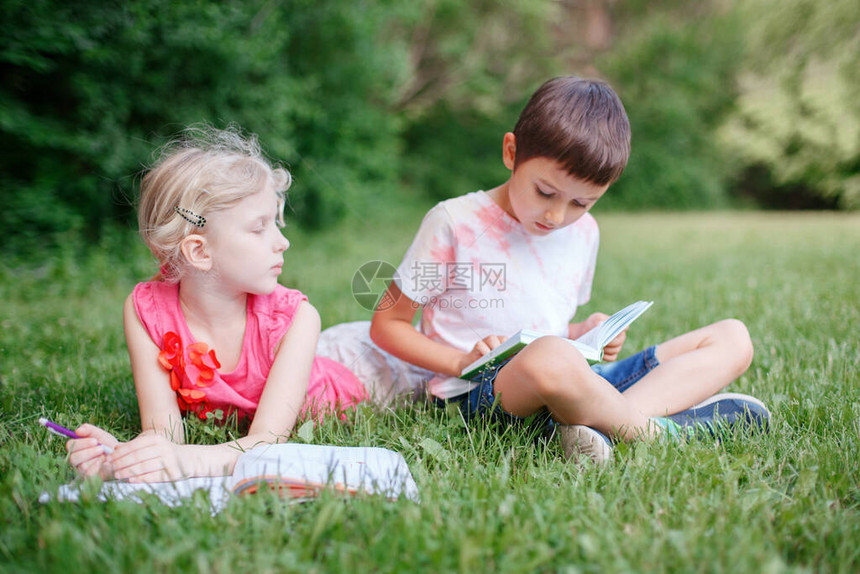 年轻的白种人学校女孩和男孩朋友在户外公园做作业孩子们看书和用铅笔写字儿童教育图片