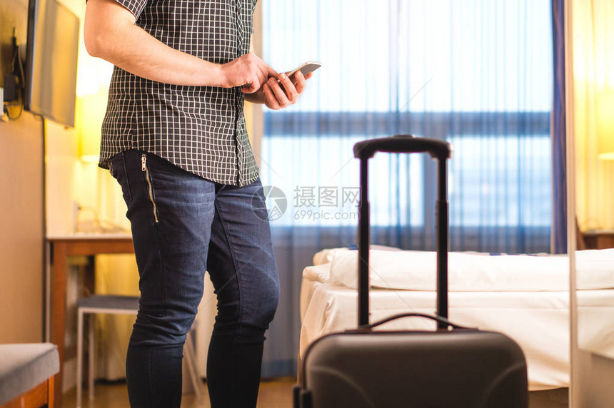 男子在带行李和手提箱的酒店房间里使用智能手机在度假出租公寓里带手机的游客叫出租车或在线办理登机手续旅行和图片