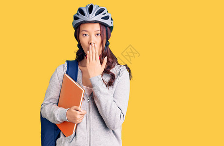 身着学生背包和自行车头盔的年轻女孩手持书本图片