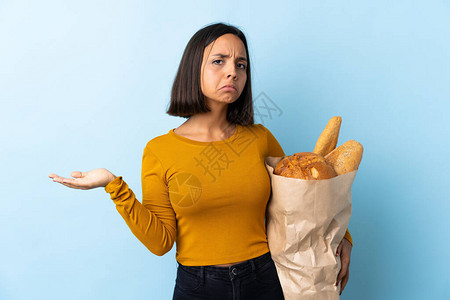 年轻的拉丁女人买一些面包孤立在蓝背景的蓝色背景做图片
