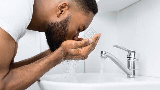 年轻Afro男人在浴室洗脸池洗图片
