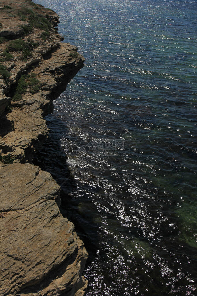 以闪亮的海面为背景的岩石海岸图片