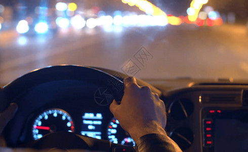 城市中的交通灯模糊把男人的手放在方向盘上仪表板在汽车的图片