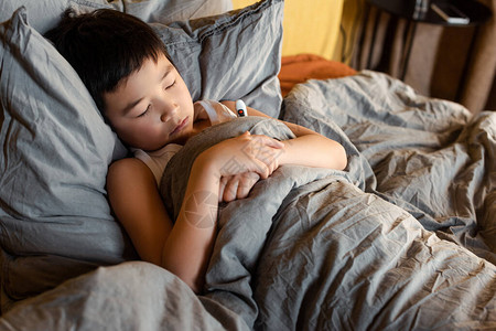 有温度计睡在床上且与自己隔离的亚洲男孩身患重图片