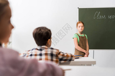 在黑板和同学旁边站立的心烦意乱的女学生有图片