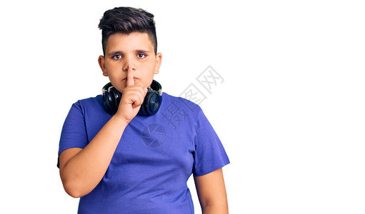 听音乐时戴耳机的小男孩要求用手指在嘴唇上保持安静沉默和秘密概念图片