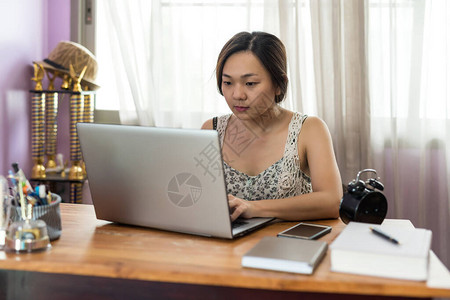 年轻的亚洲女商人在笔记本电脑上的房子类型与在桌子上工作的公司应用程序图片
