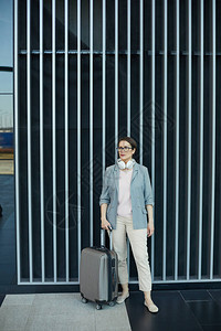 戴着白色有线耳机的严肃迷人的商务女士站在现代机场图片