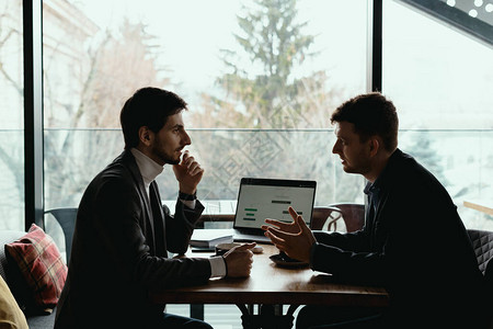 基装报价两位商人谈论在书桌用笔记本电脑规划项目考虑商业报价分享想法等新机会背景