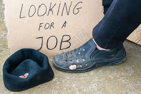 失业概念男子穿着破旧的鞋子坐在他脚边的纸板标志上图片