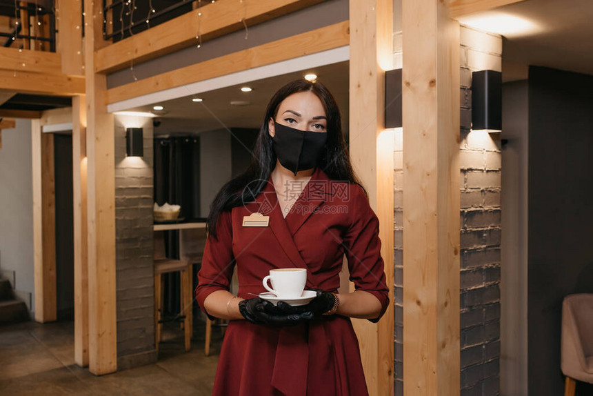 一位戴着黑色面罩和一次手套的华丽女餐厅经理正在餐厅里端着一杯咖啡一位穿着红宝石连衣裙的好心的咖啡馆老板图片