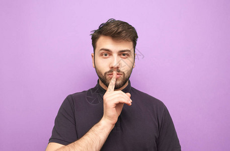 身穿紫色背景深色T恤的男人把手指放在嘴边图片