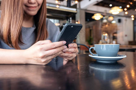 一位妇女拿着并使用智能手机桌上有咖啡杯的妇图片