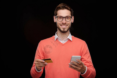 用信卡和智能手机站立并使用在线交易服务的快乐英俊图片