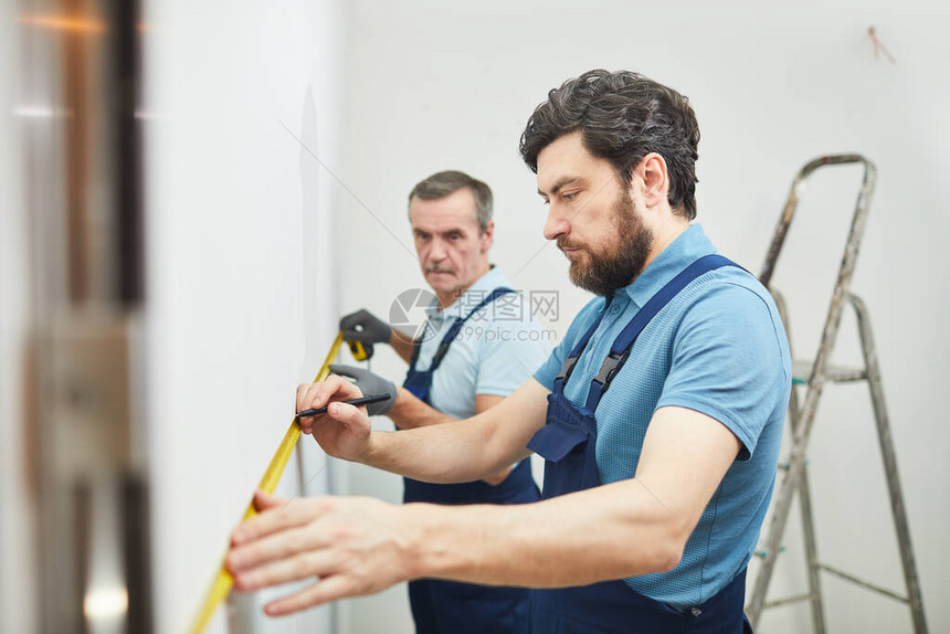 两名建筑工人在翻修房屋和复制空间时测量墙壁的侧面图片