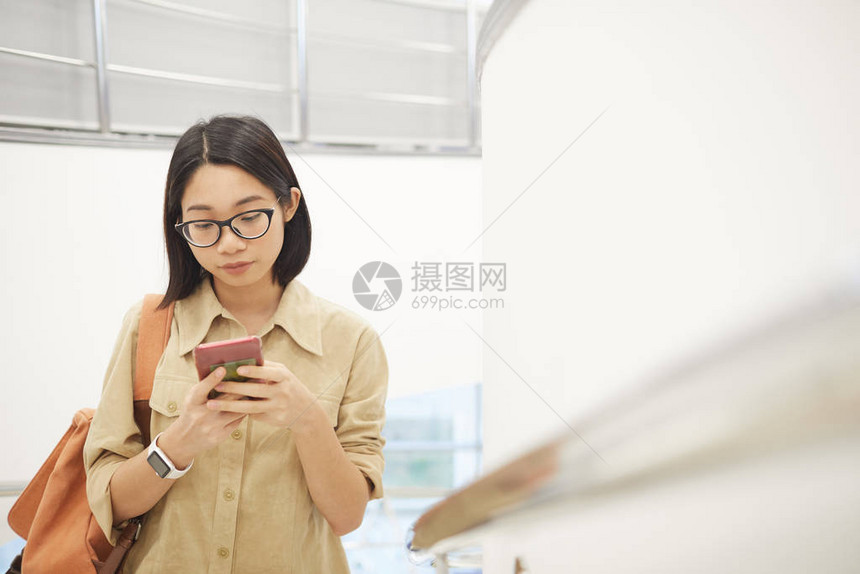 现代大学室内楼梯上使用智能手机的年轻亚洲女腰部肖图片