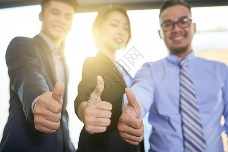 三名现代商界人士在摄影机前微笑时举起拇指手势图片