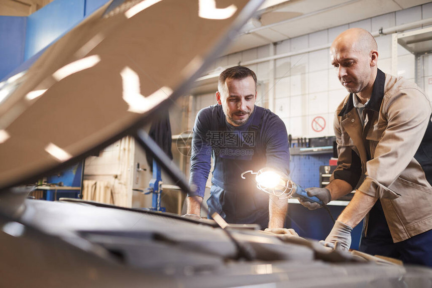 两名汽车修理工在汽车修理厂的汽车引擎盖下看腰部肖图片