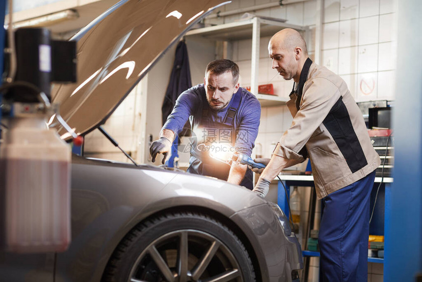 两名汽车修理工在汽车维修车间看汽车引擎盖下的肖图片
