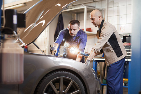 两名汽车修理工在汽车维修车间看汽车引擎盖下的肖图片