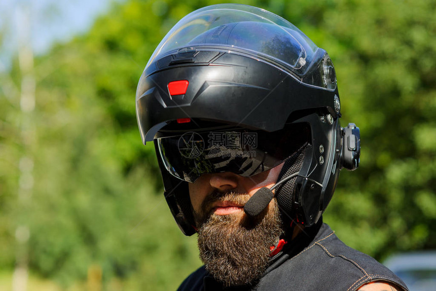 戴着头盔的胡子的男人摩托车赛季开幕骑自行车的人在木头与绿色的树叶背景上春天Bikers摩托车手头部保护戴头盔的特写面图片