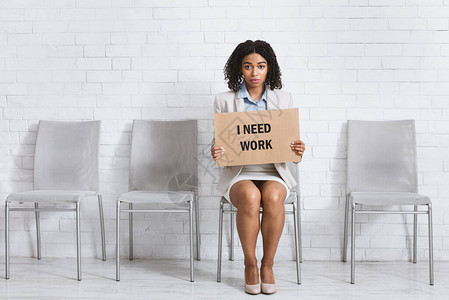 绝望的黑人女士在公司办公室等待就业面试时举着我需要工作的牌图片